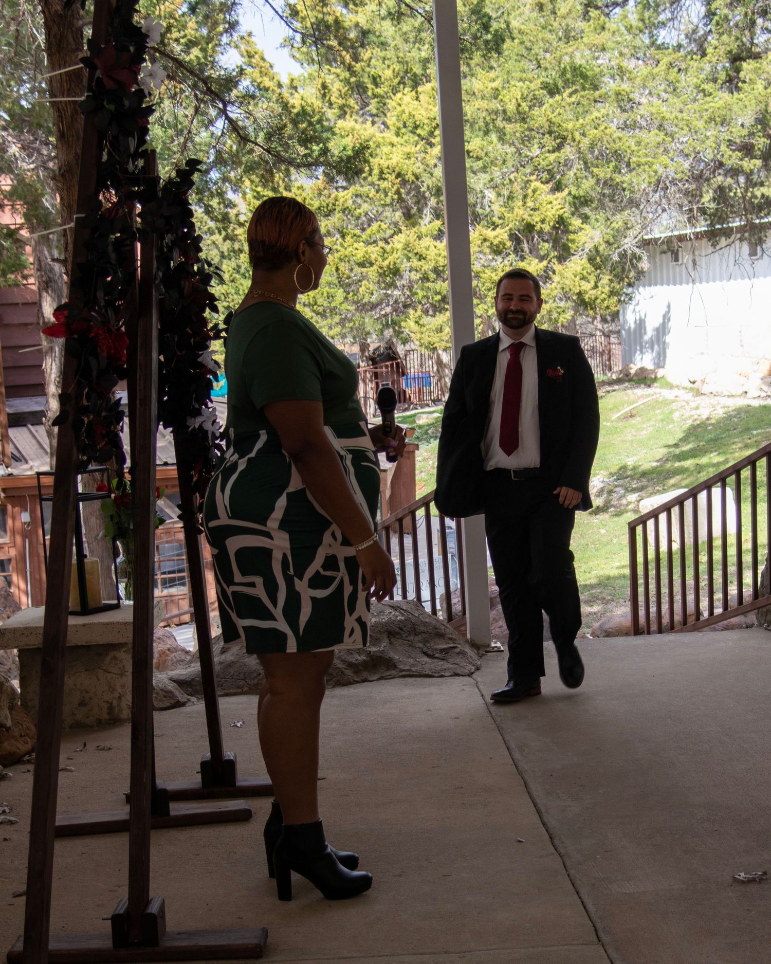 Two people having a conversation in a covered outdoor walkway with trees visible in the background.