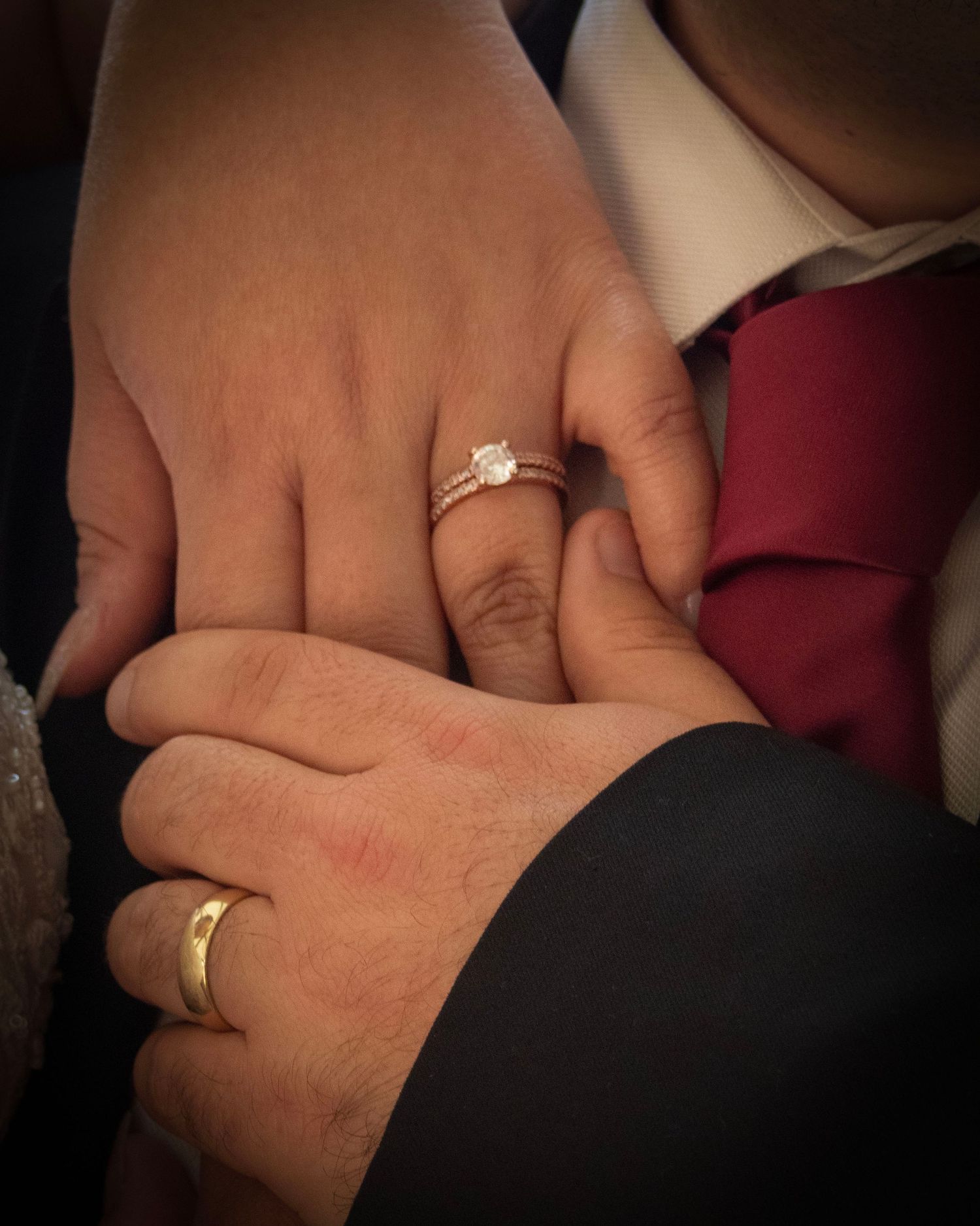 Close-up of two hands displaying wedding rings and engagement ring against formal attire.