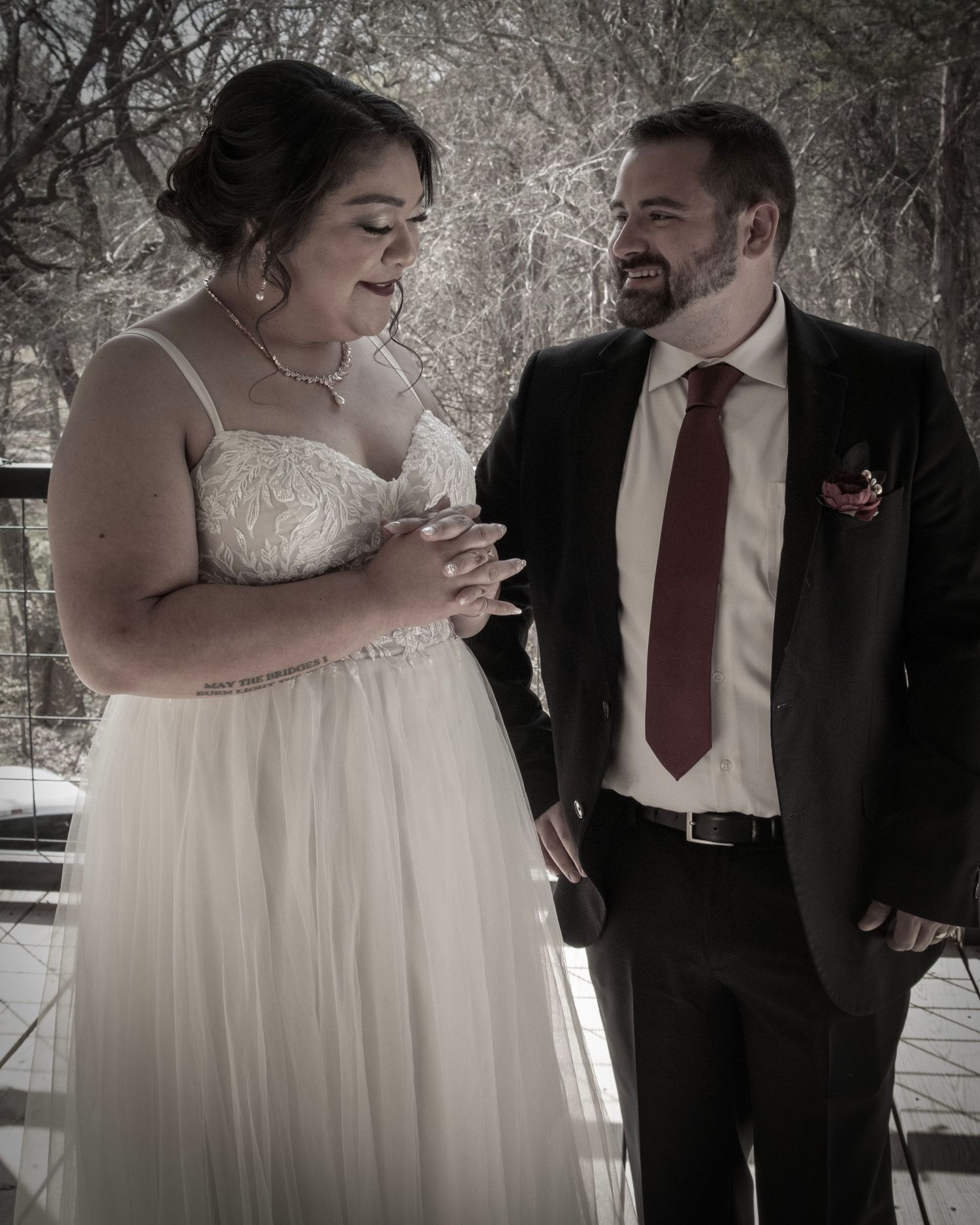 Bride in white lace dress and groom in dark suit share intimate moment during outdoor wedding photoshoot.