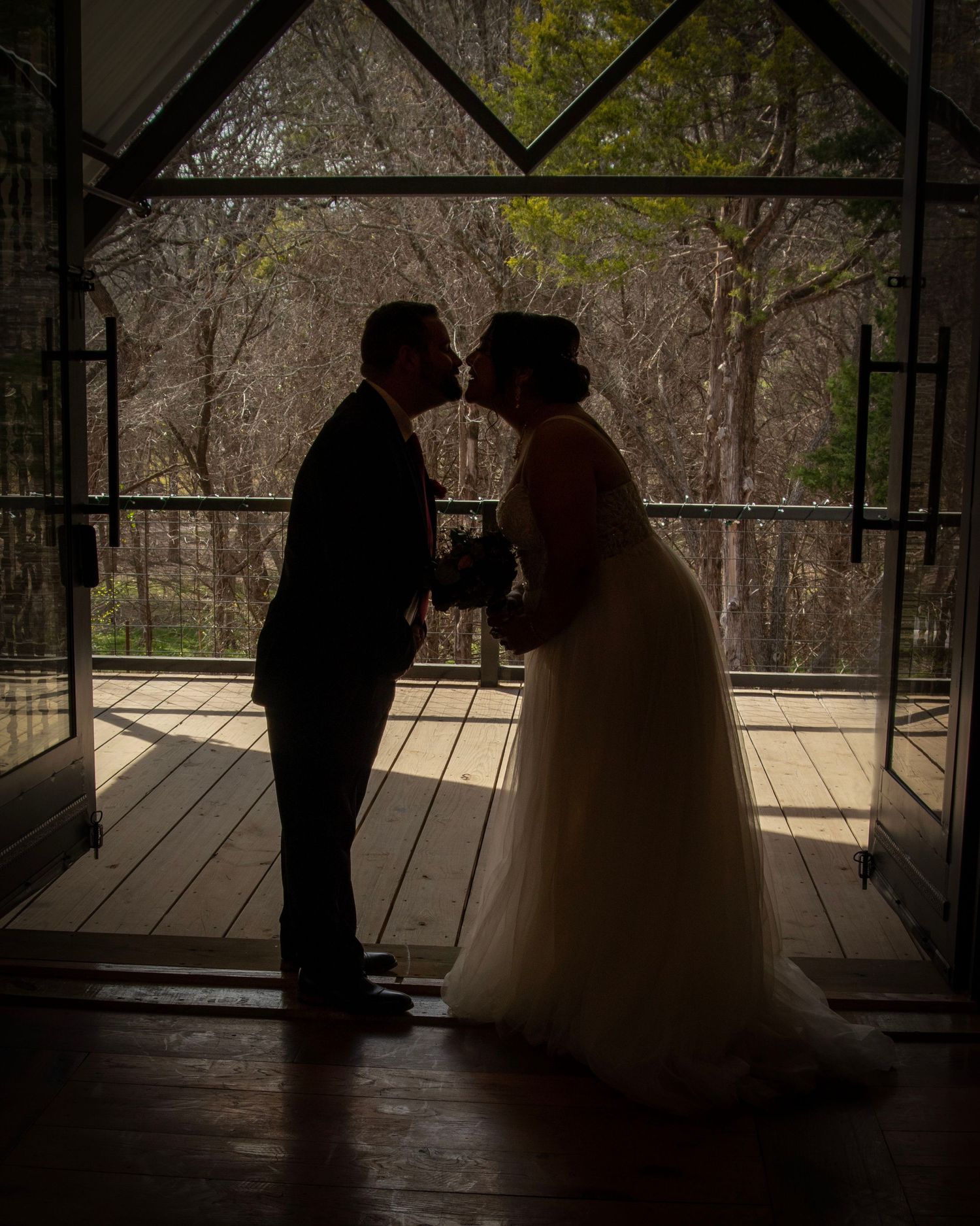 A silhouetted couple shares an intimate moment on a covered porch with natural lighting behind them.