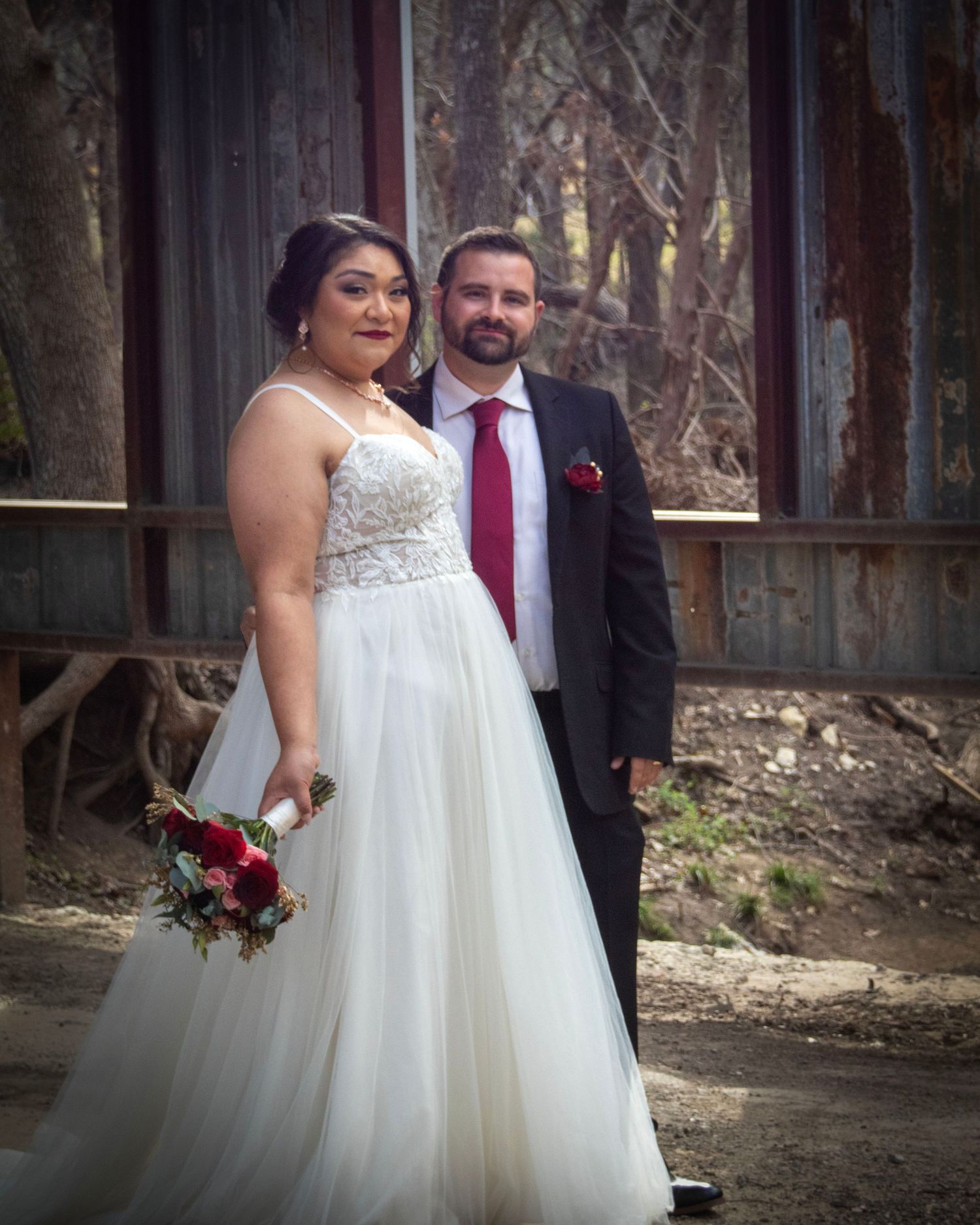 A couple stands together on their wedding day in front of a rustic barn backdrop.