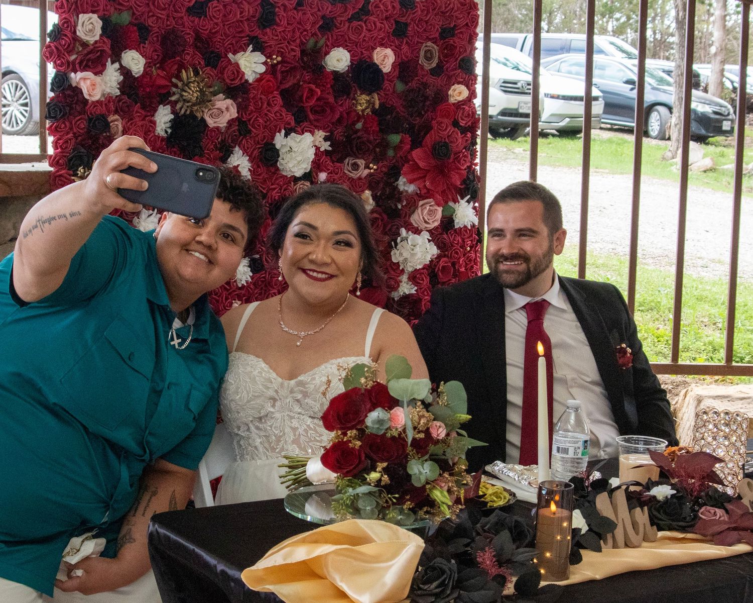 Wedding party enjoying a meal at a table decorated with red roses and floral arrangements.