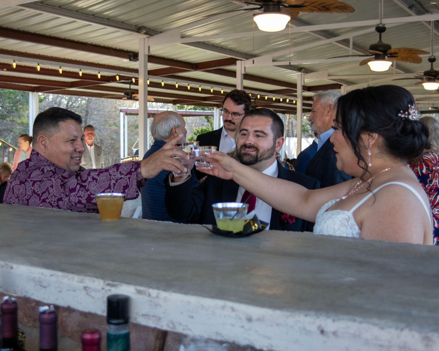 Wedding celebration at an outdoor reception bar with guests toasting.