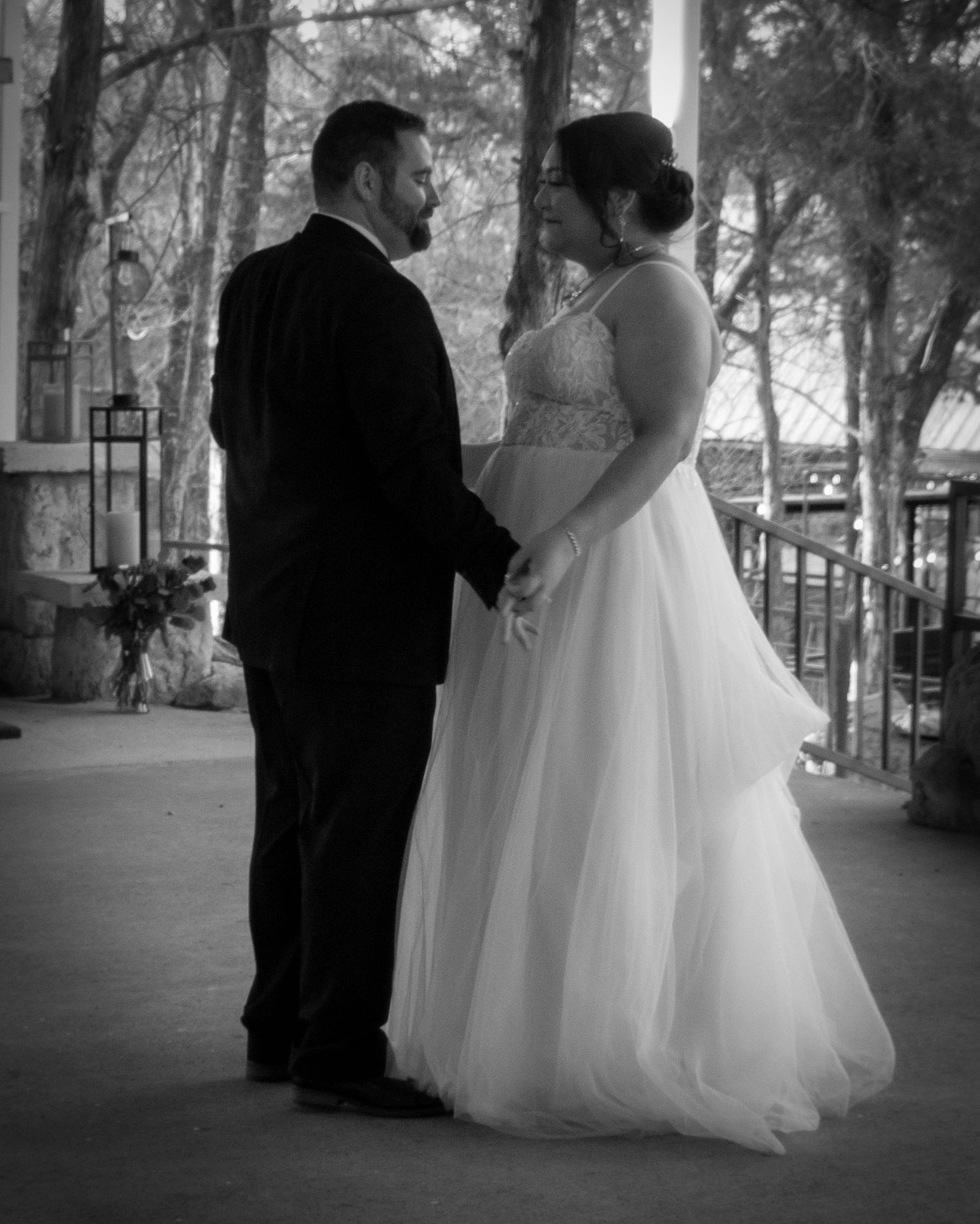 A black and white wedding photo of a couple in formal attire standing together under a covered outdoor area.
