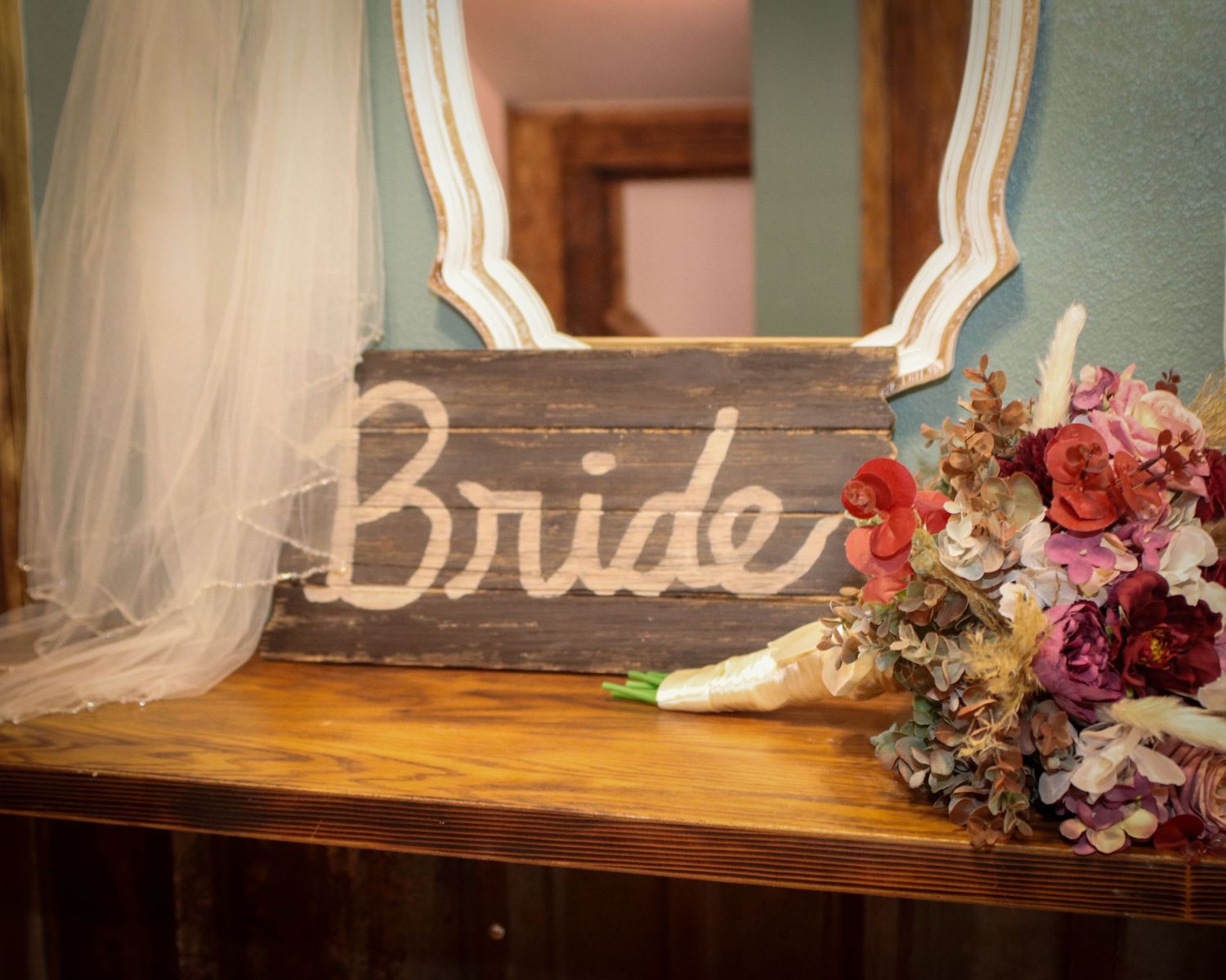 Rustic wooden bride sign displayed with colorful flowers and bridal veil on wooden table with vintage mirror.