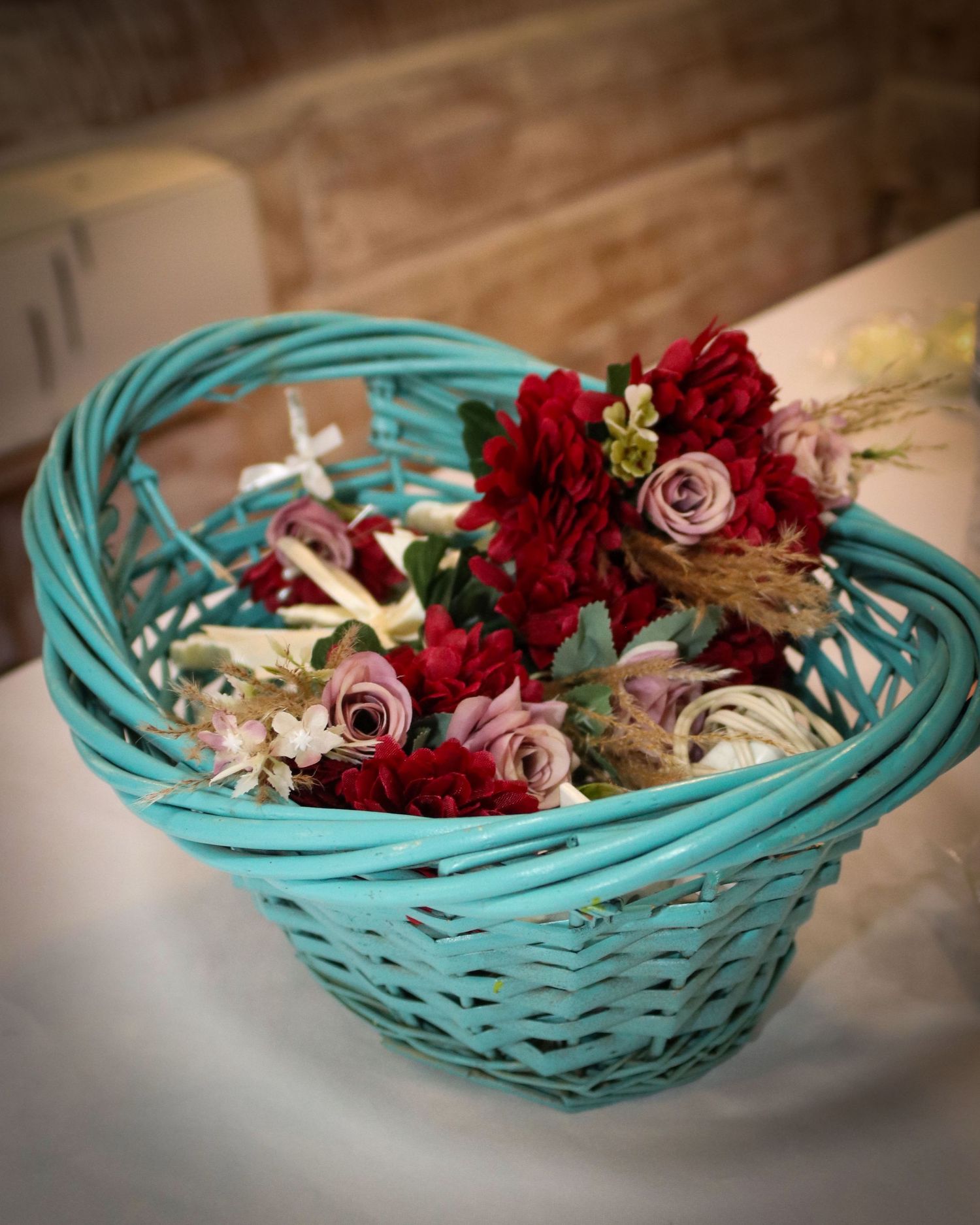 A turquoise woven basket filled with red and pink roses and dried flowers arranged in a rustic style.