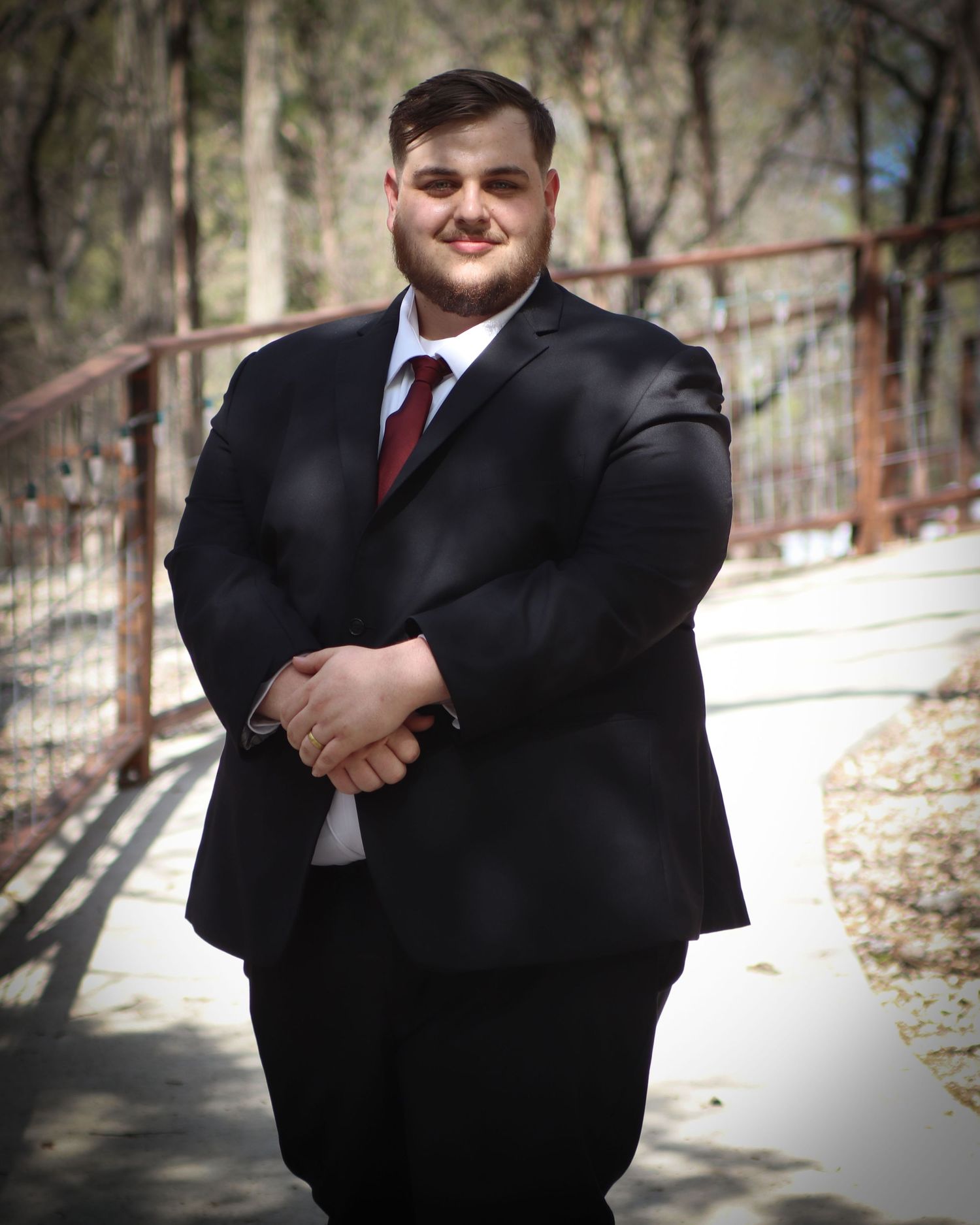 Professional portrait of someone in a dark business suit and red tie standing on a winding outdoor walkway.