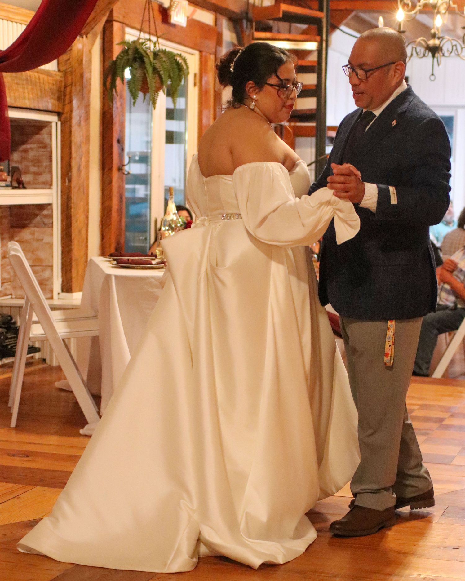A tender wedding dance moment between a couple in a rustic venue with wooden decor and hanging plants.