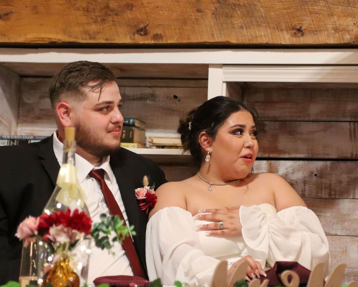 A casual wedding reception scene with a couple sitting together at a decorated table with rustic wooden walls.
