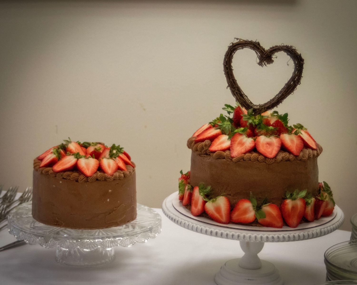 Two chocolate cakes decorated with fresh strawberries and a heart-shaped topper on display for a romantic occasion.