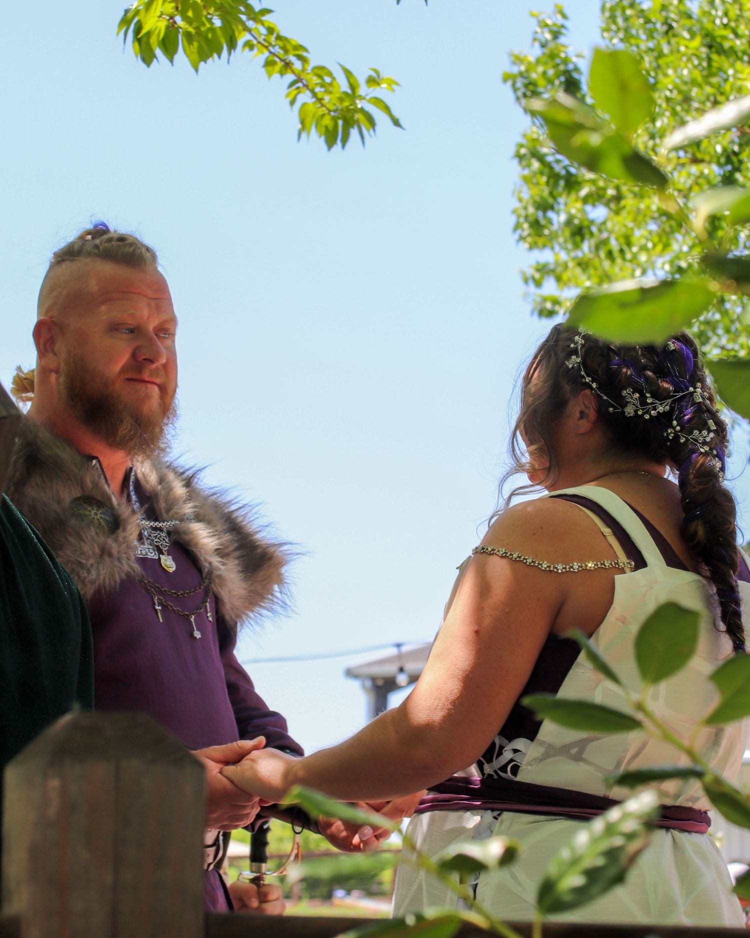 A wedding ceremony takes place outdoors under green leaves in natural sunlight.