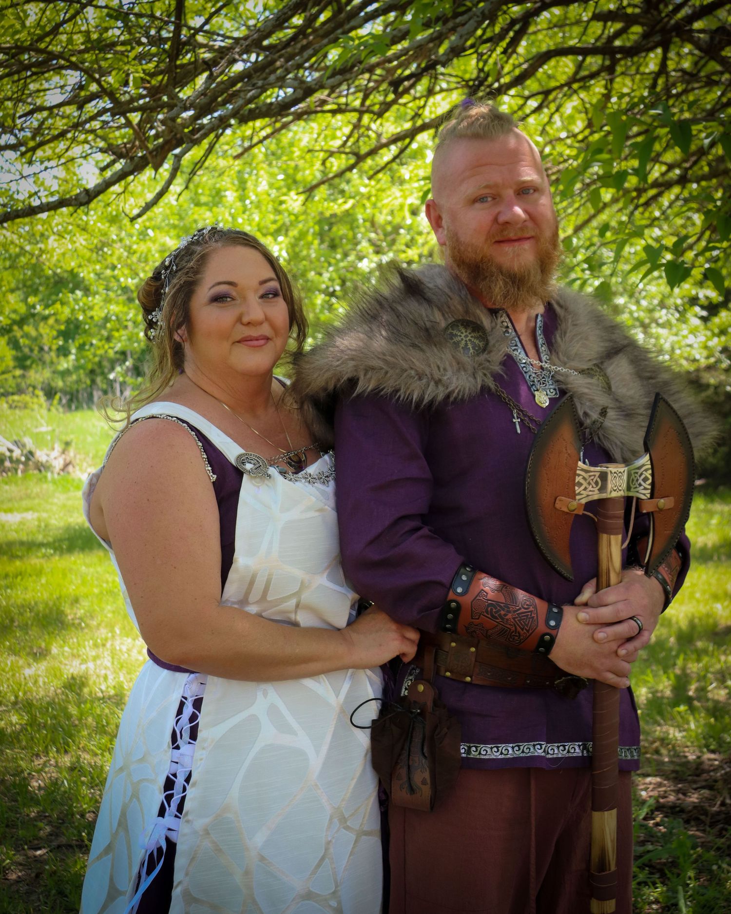 Medieval themed wedding portrait with purple and brown viking attire and white dress in a garden setting.