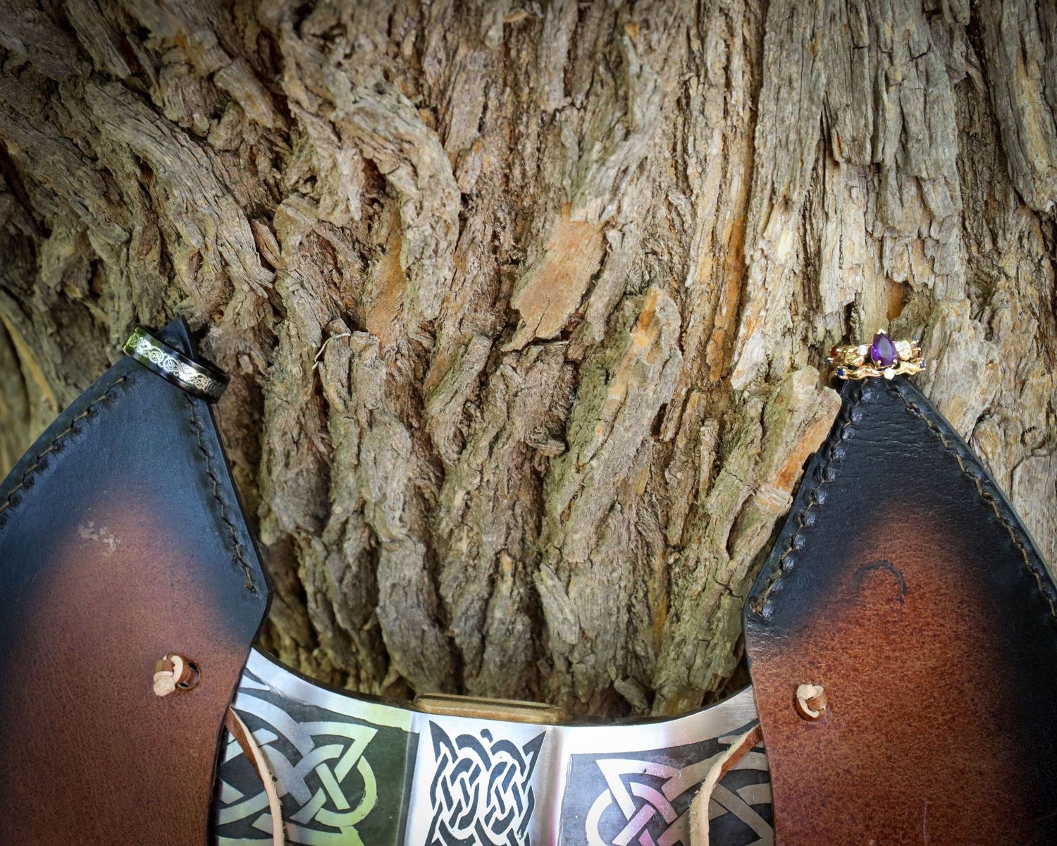 Close-up view of leather boots with Celtic design details against textured tree bark background.