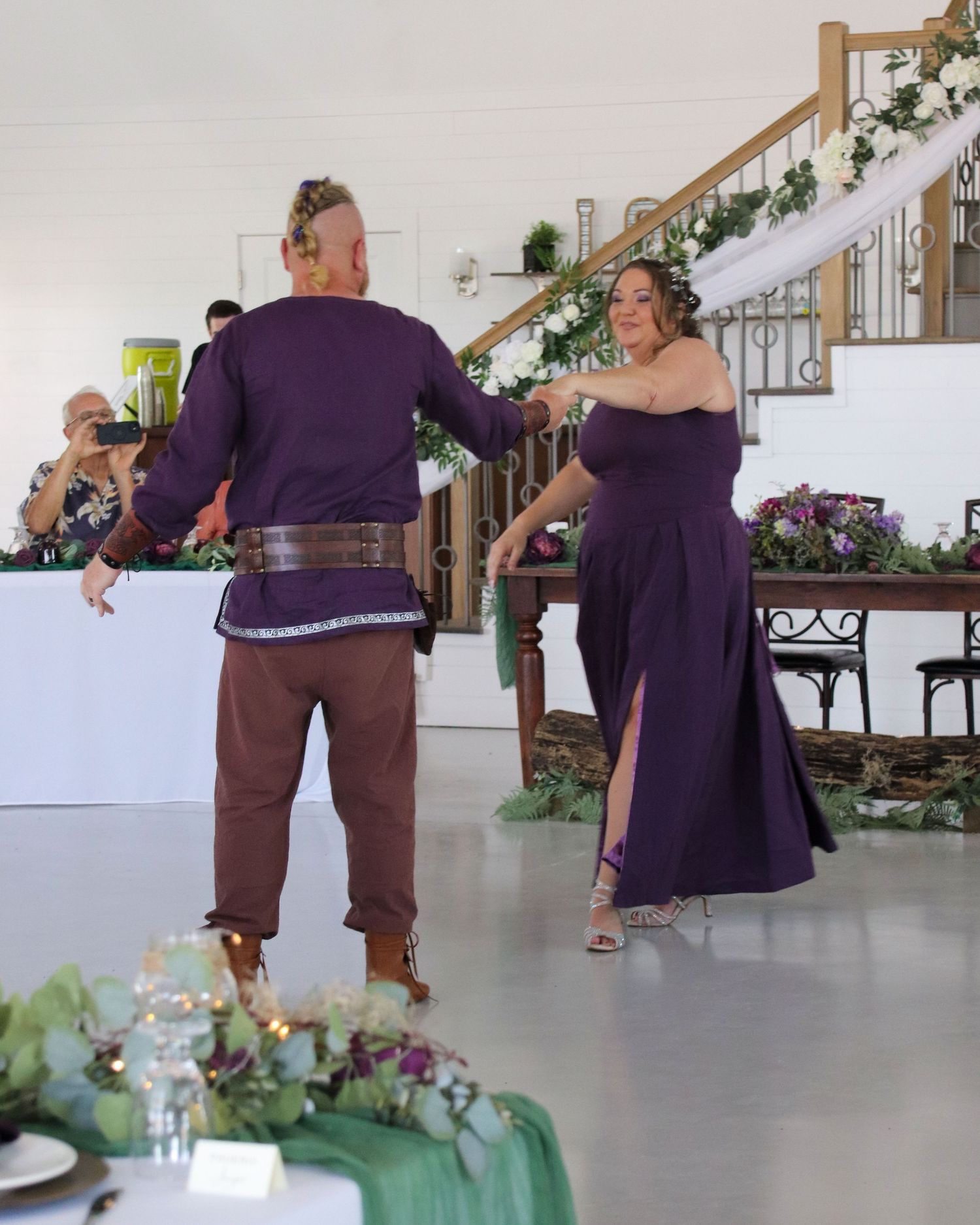 Wedding couple in coordinating purple outfits dancing in a decorated reception venue.