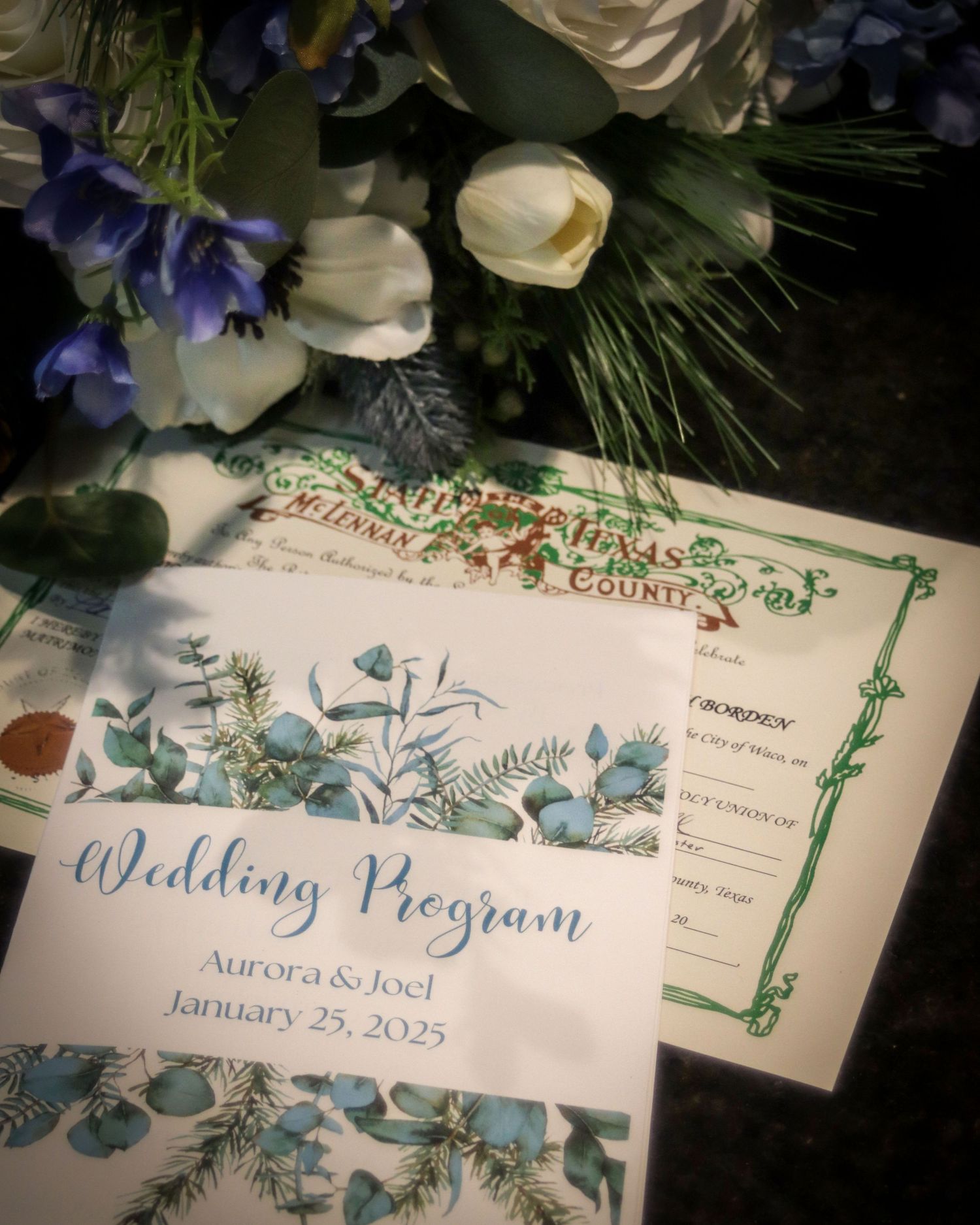Wedding program with delicate blue floral designs and greenery borders displayed alongside white and blue flowers.