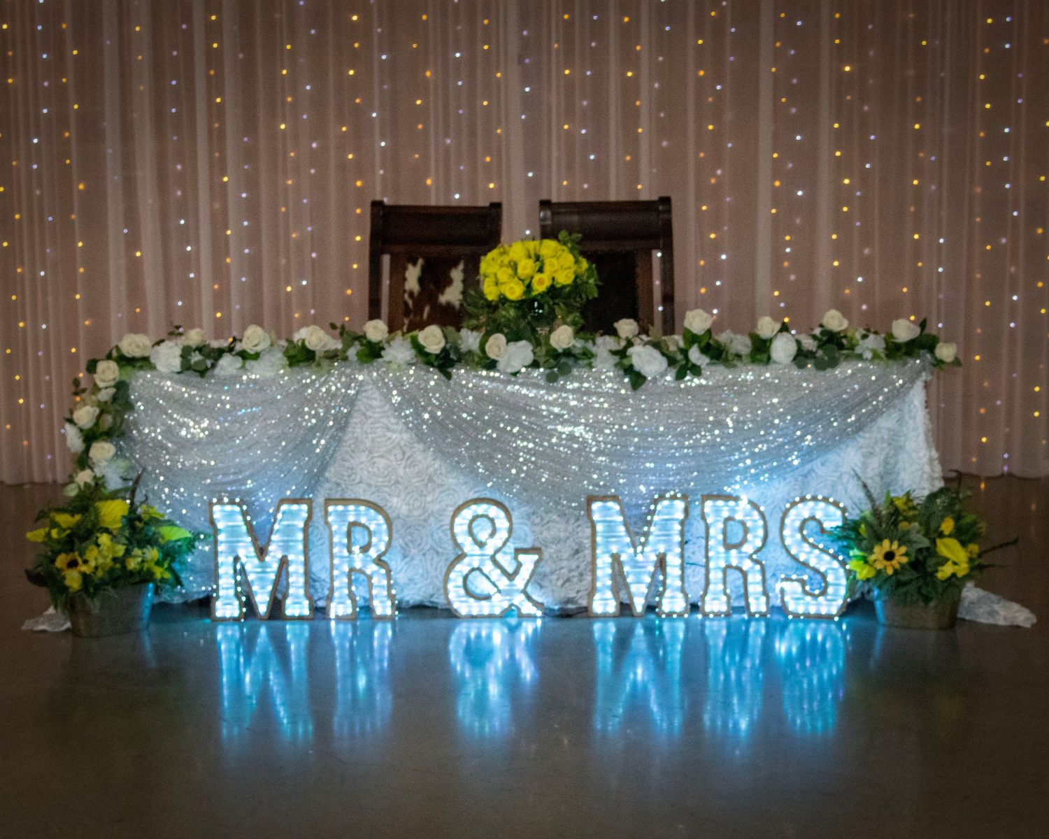 Illuminated blue 'MR & MRS' sign with twinkling lights and floral decorations at a wedding reception.