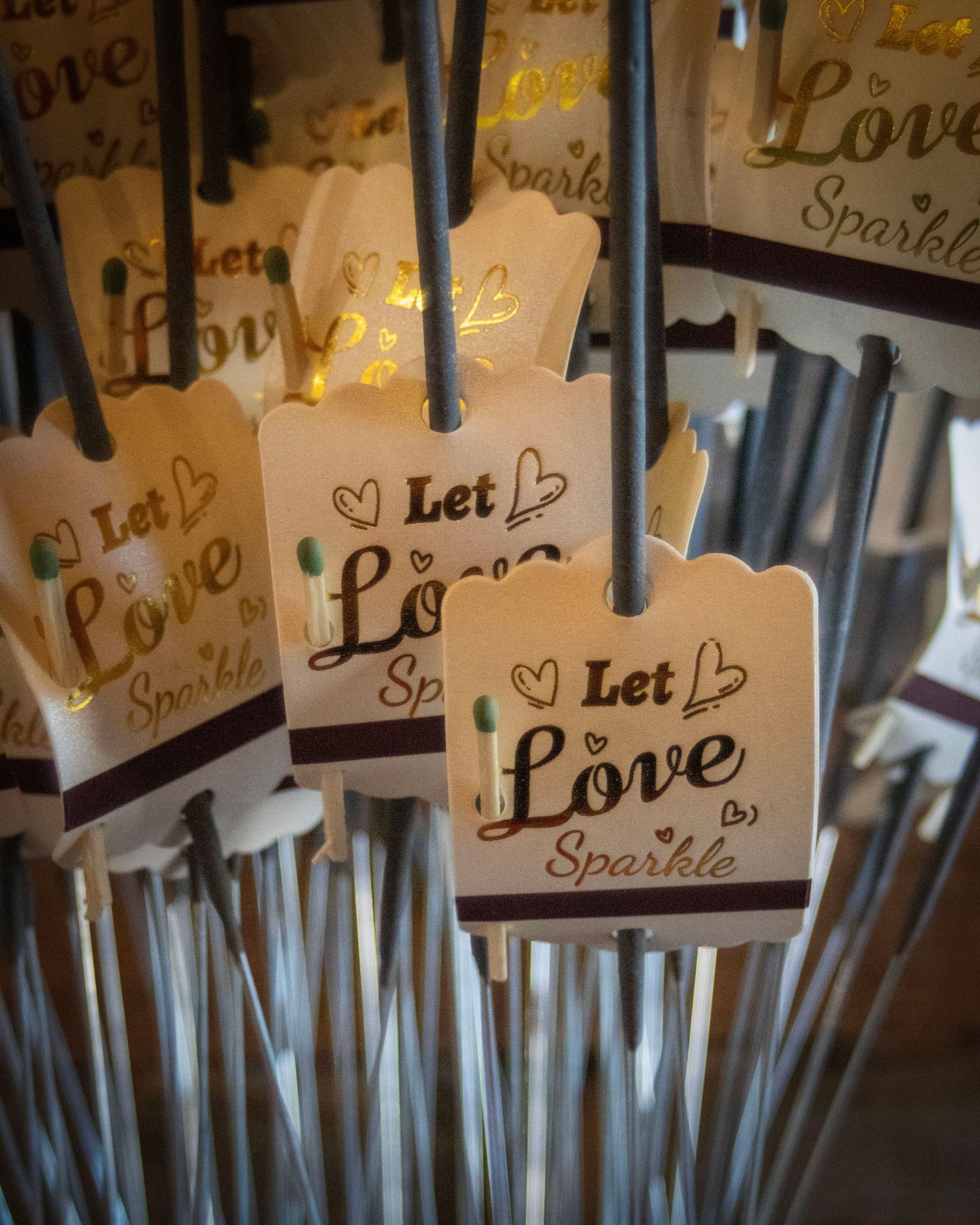 Wedding sparklers with decorative tags reading 'Let Love Sparkle' displayed in a bundle with warm lighting.