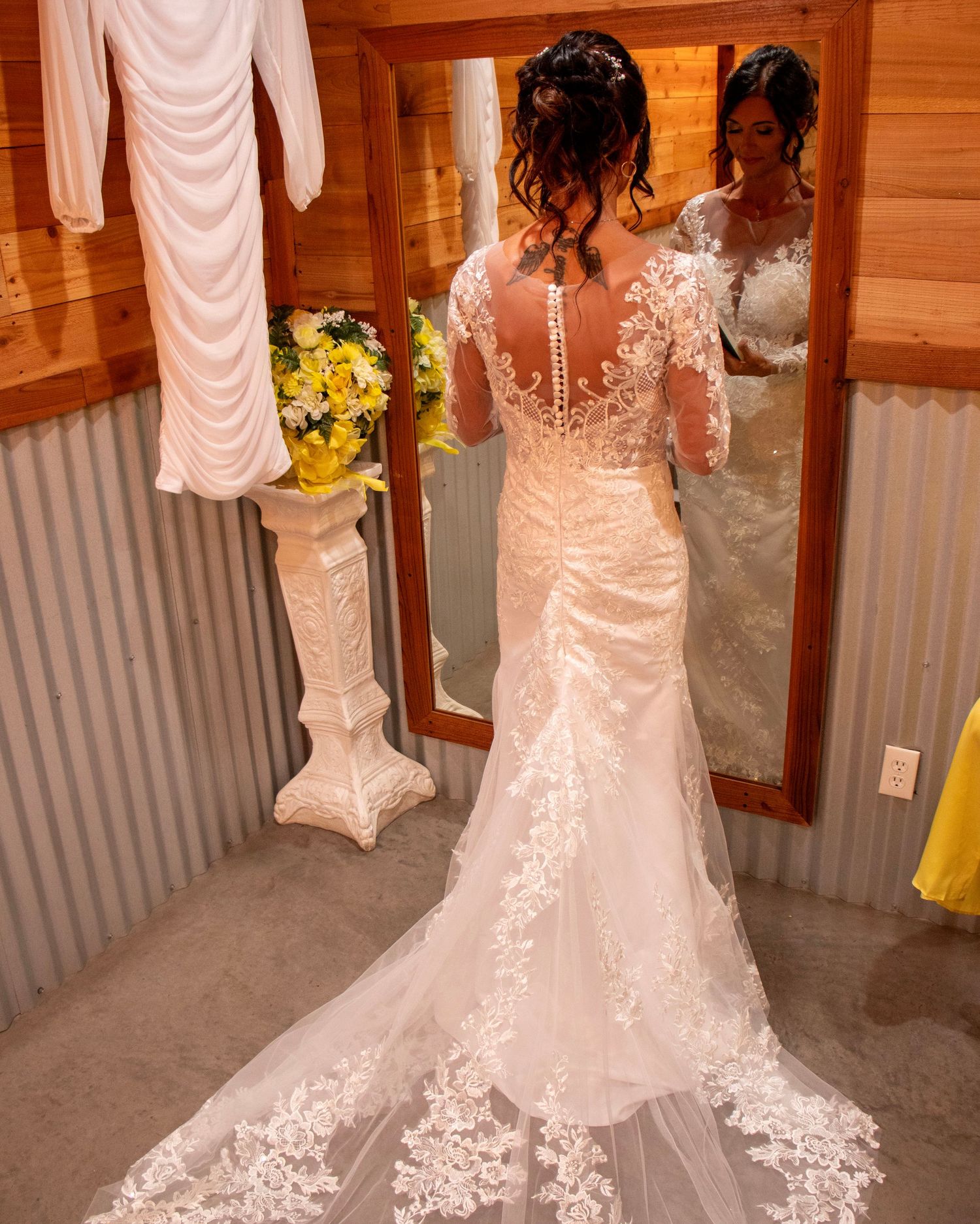 Back view of elegant lace wedding dress with sheer illusion panel and floral appliques shown in rustic dressing room.