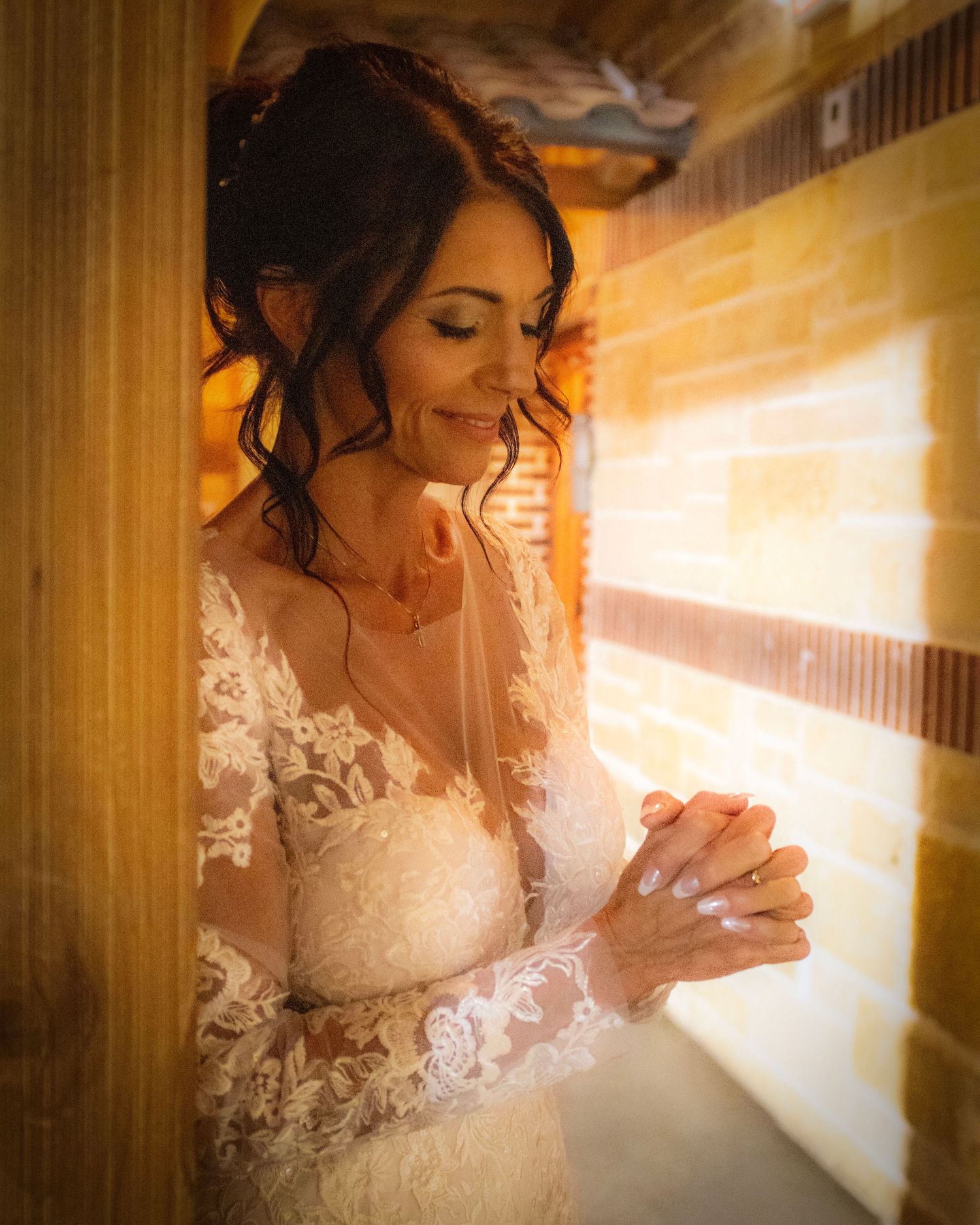 Warm sunlight streams through window onto delicate lace wedding gown in an intimate moment.