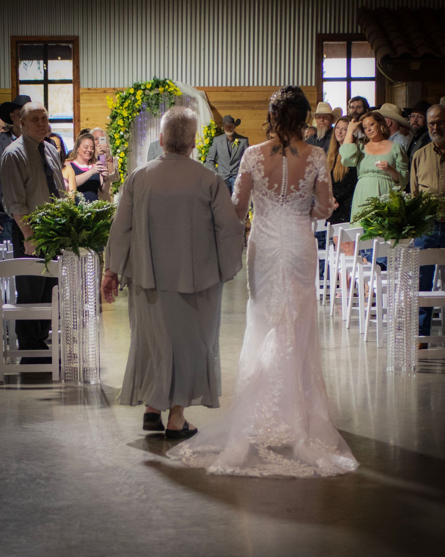 A wedding ceremony in progress in an industrial-style venue with a floral arch and white chairs.
