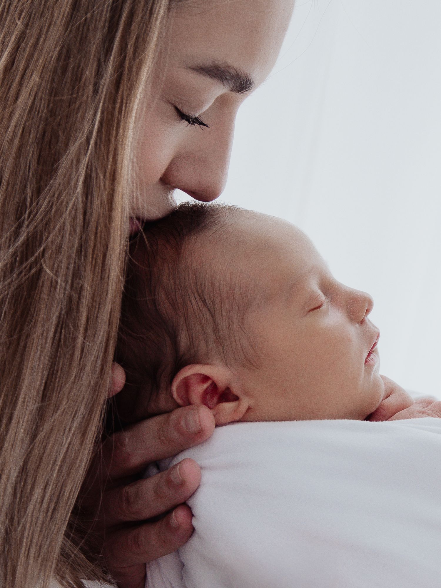 A peaceful sleeping newborn wrapped in soft white fabric wearing a delicate pink headband rests serenely.