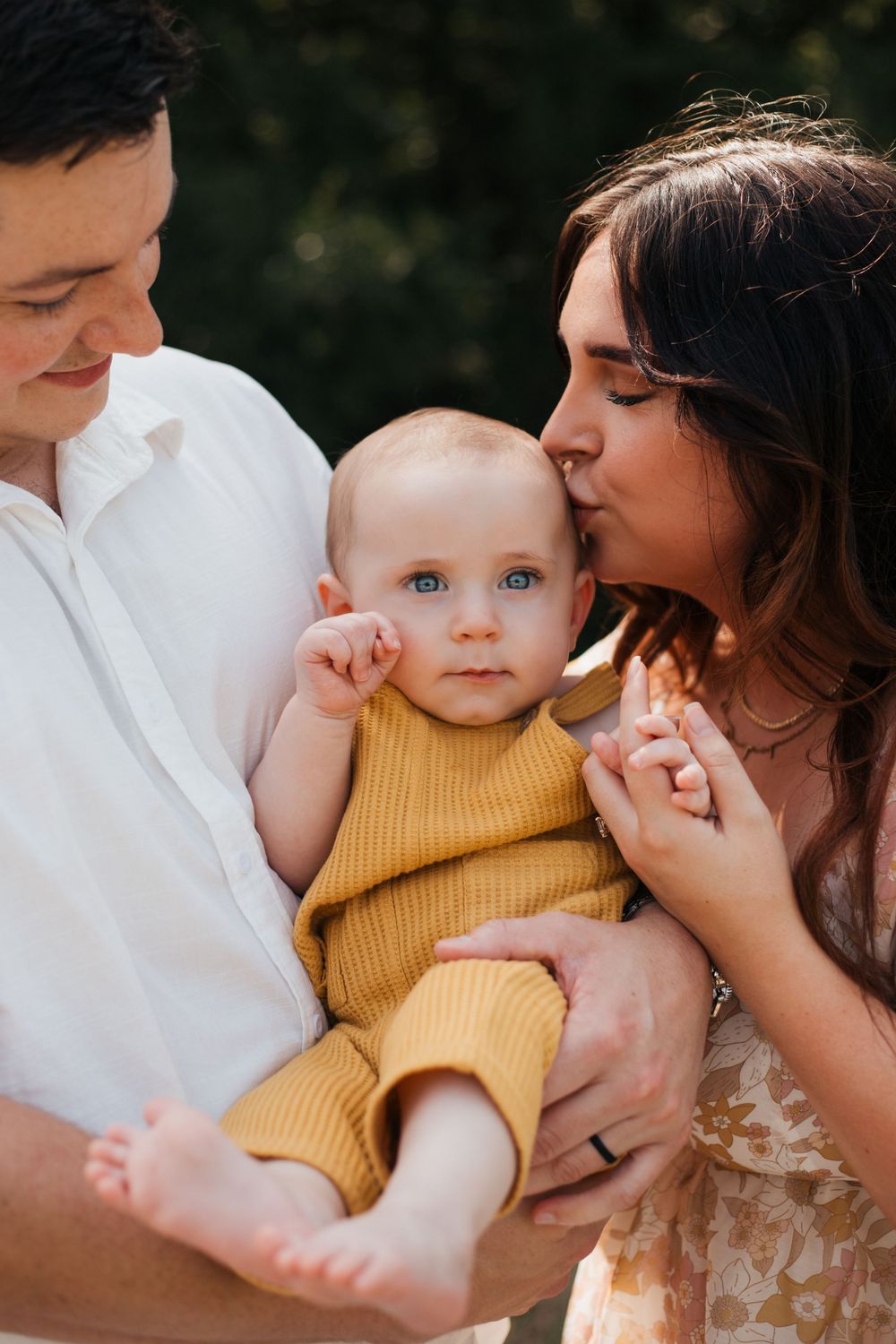 Sweet family moment with baby in yellow romper being cuddled by parents.
