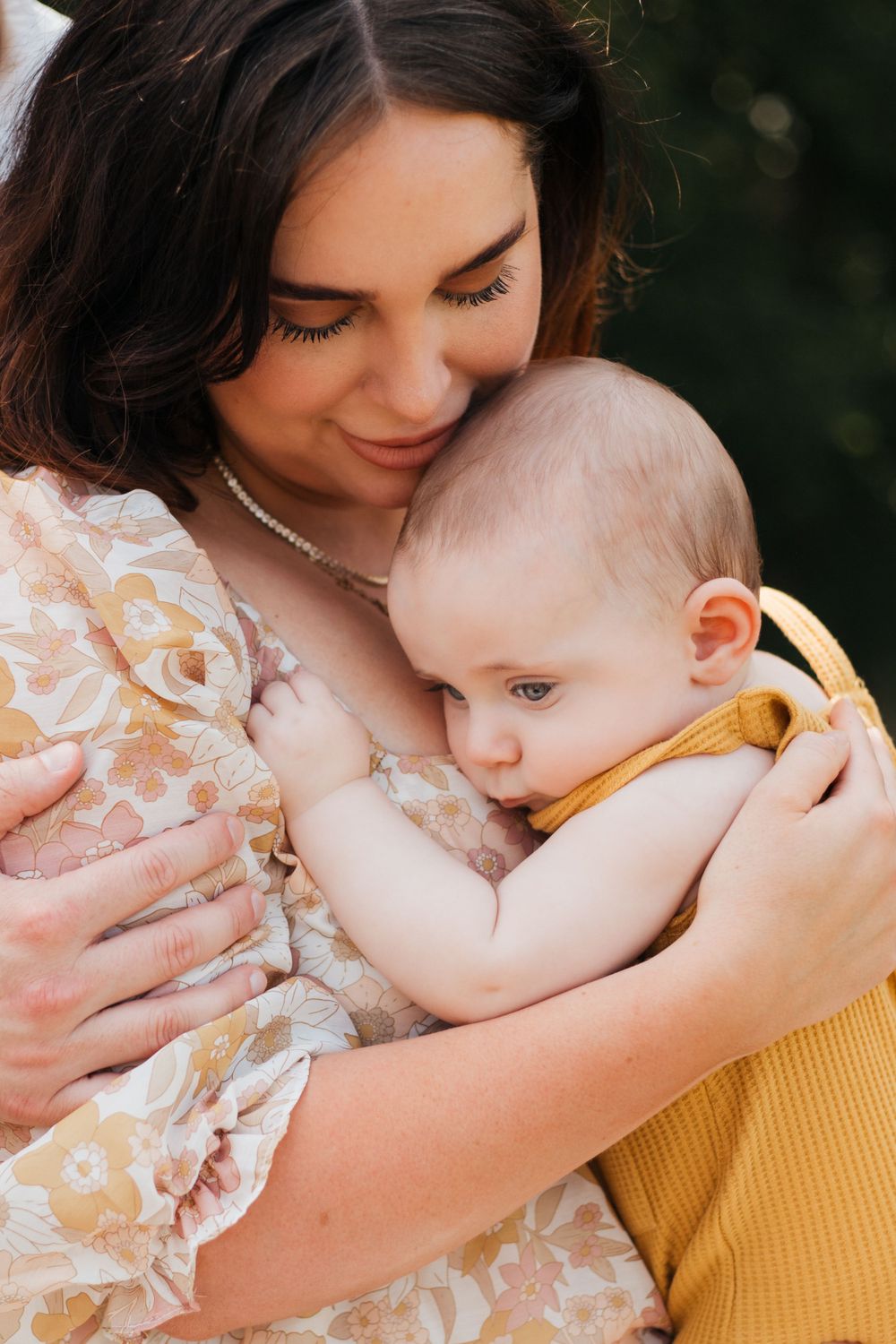 Intimate motherhood portrait showing tender embrace with baby in yellow romper.