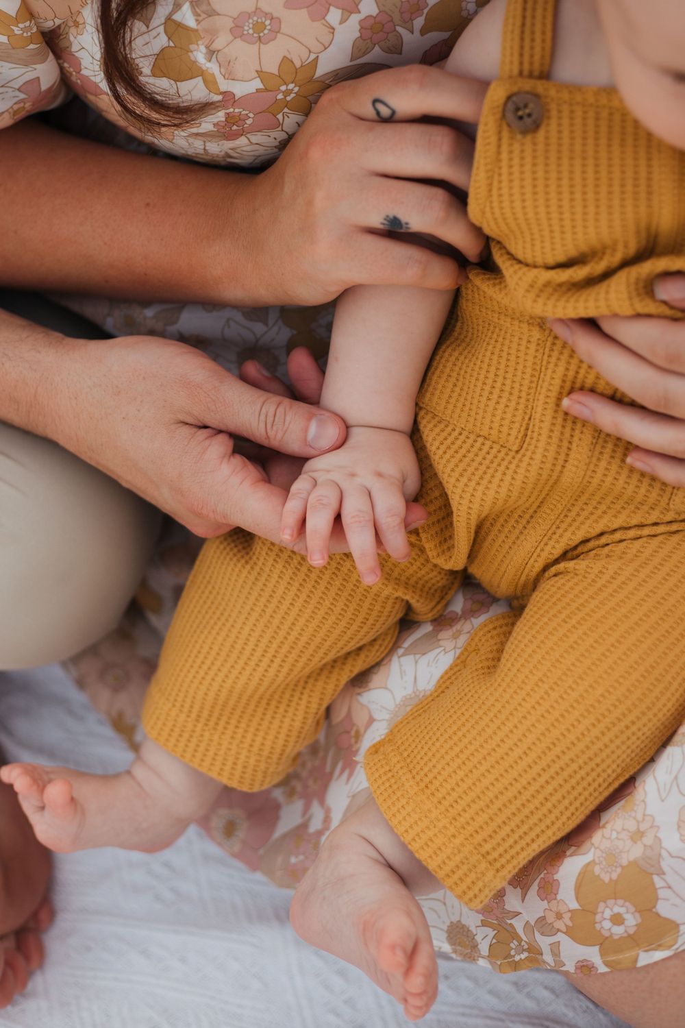 Close-up of tiny baby hands being held while wearing a mustard yellow ribbed romper.