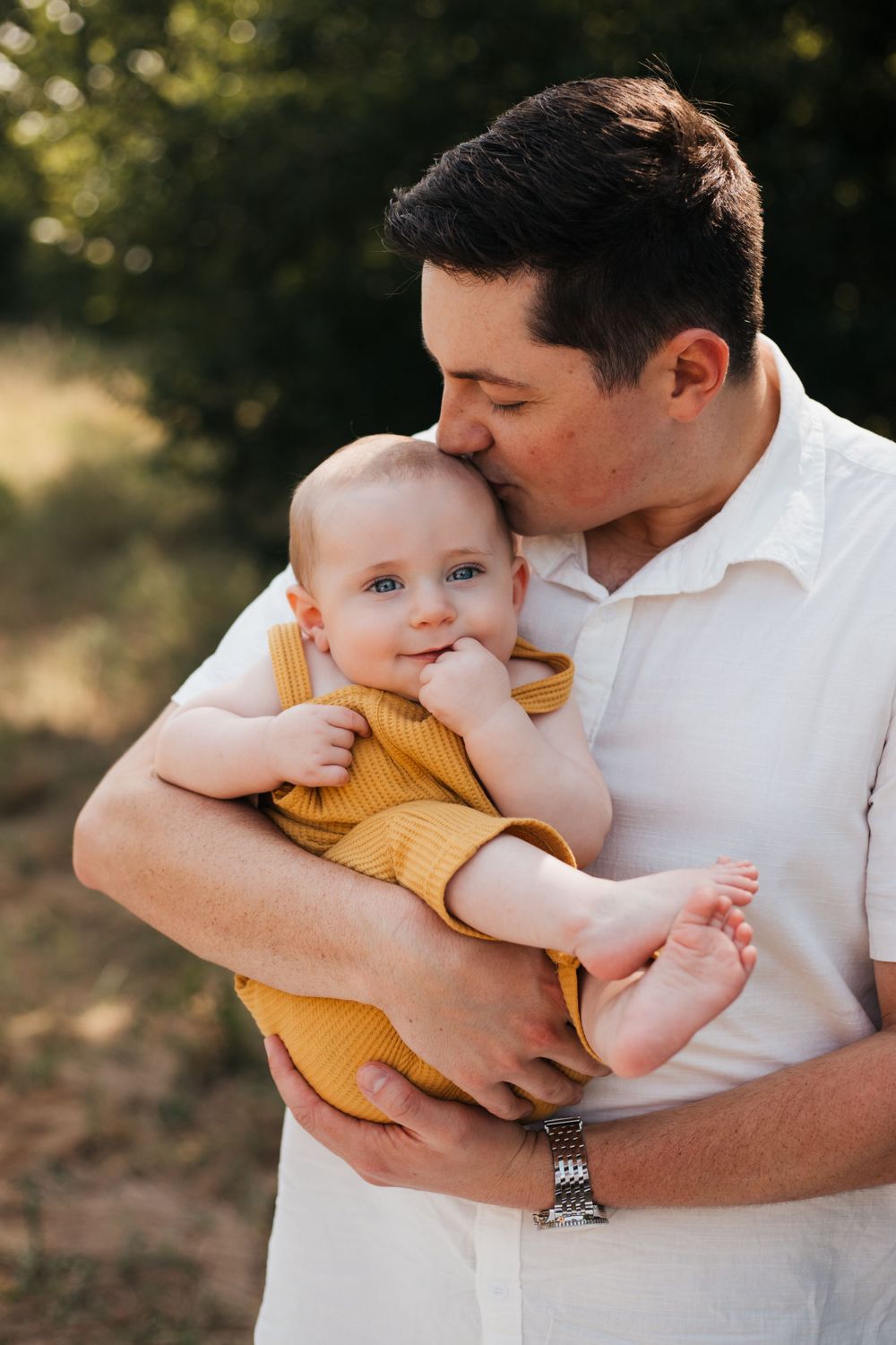 Tender moment between parent and baby wearing yellow overalls during outdoor portrait session.