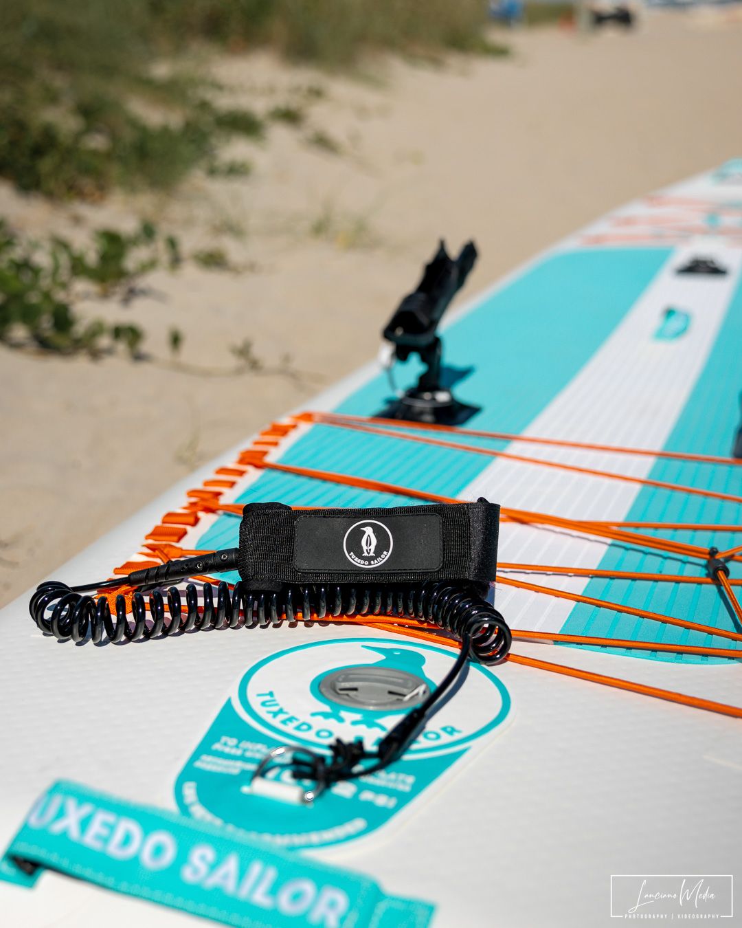 SUP board leash and mount attachment on turquoise and orange paddleboard on sandy beach.