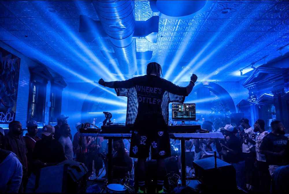 DJ performing on stage with dramatic blue light beams illuminating a packed crowd at a nightclub event.