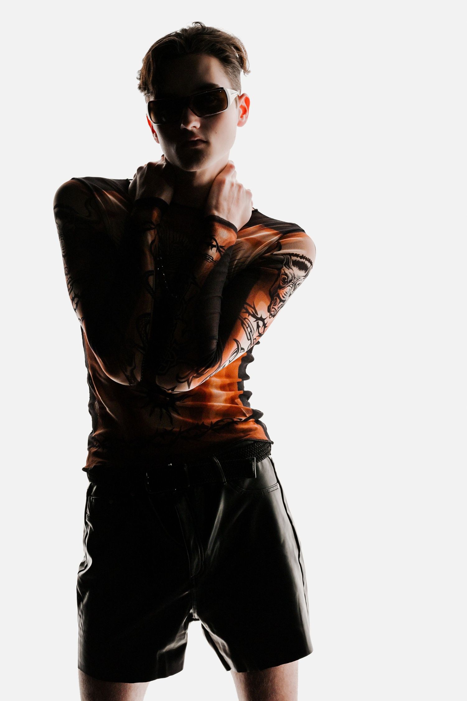 Artistic fashion portrait with dramatic lighting showing figure in brown leather top and black shorts against white background.