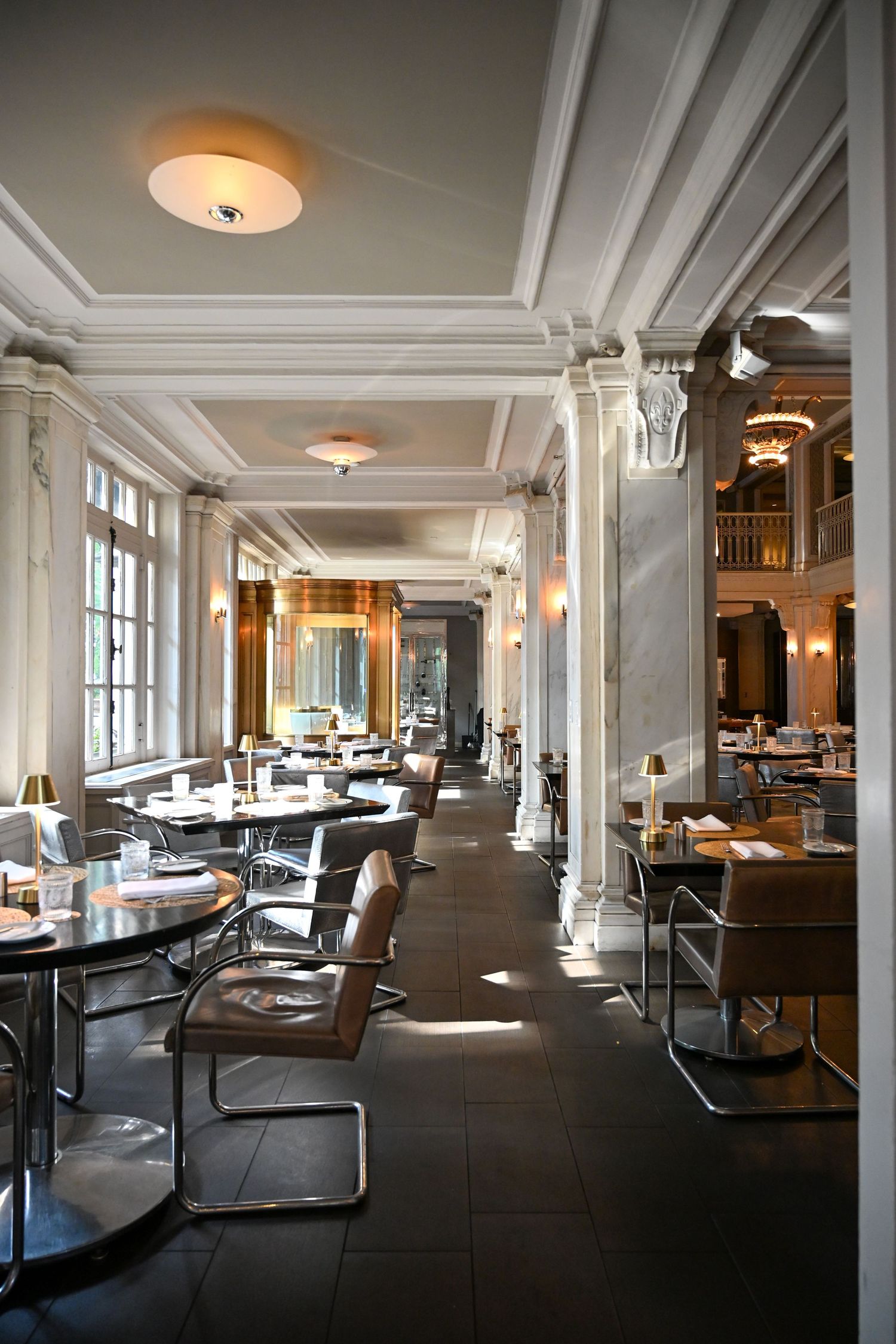 Elegant restaurant interior with white columns, dark floors, and round dining tables illuminated by warm ceiling lights.