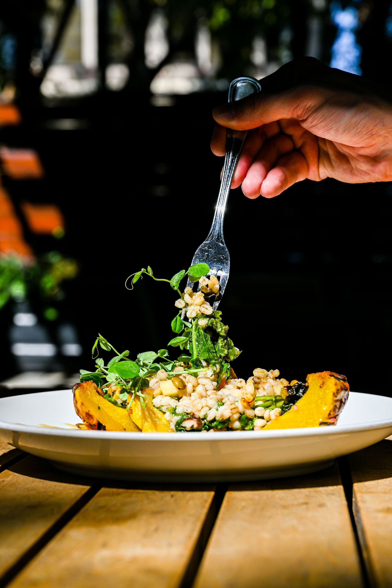 Fork lifting fresh salad from yellow squash bowl on wooden table in natural lighting.