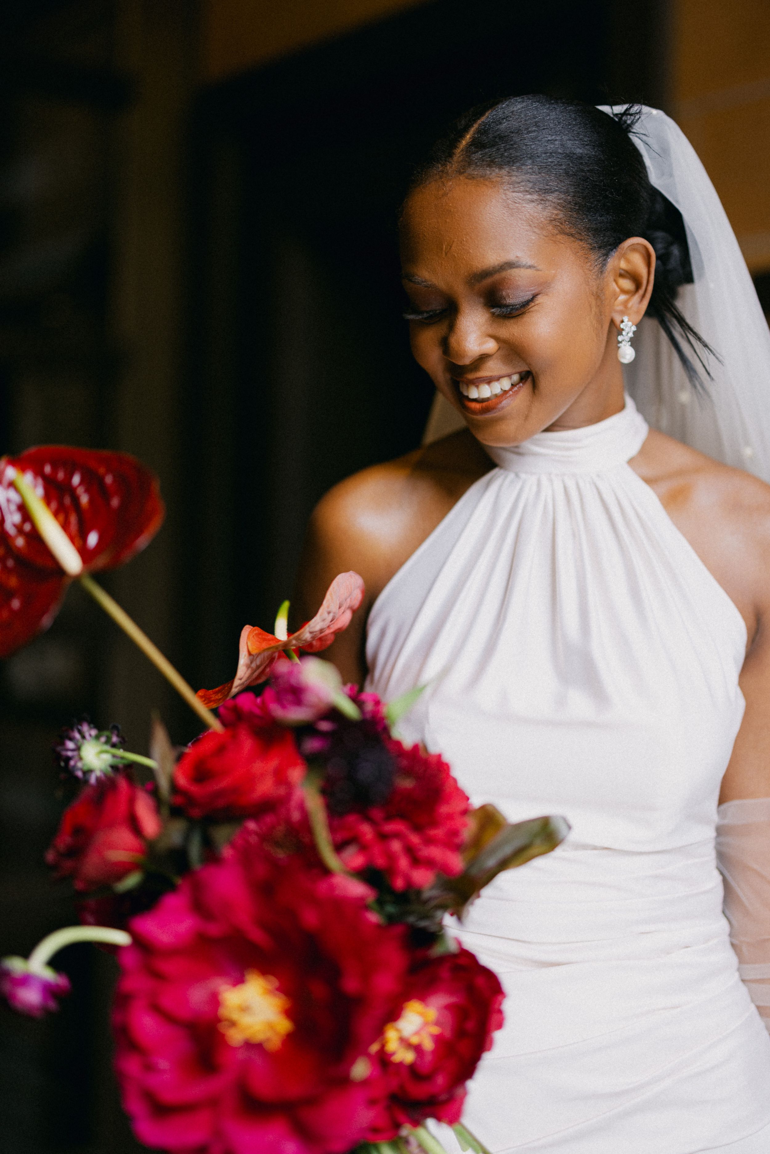 Elegant bride in white halter dress holding vibrant red bouquet.