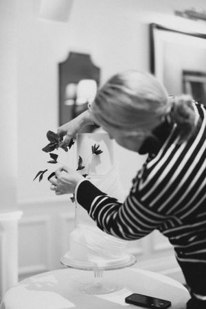 Person in striped shirt arranging flowers on a white cake stand.