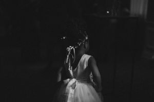 A black and white photo showing the back of a bride in a white dress with dramatic lighting.