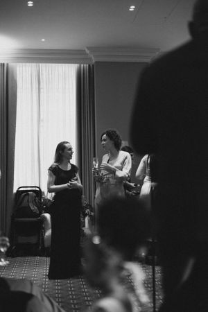 Two wedding guests in formal attire having a conversation in an elegant hotel room.