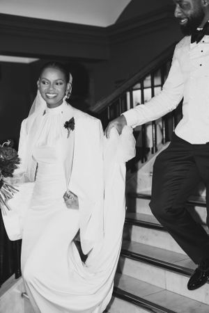 A couple in elegant white attire descending stairs during a wedding celebration.