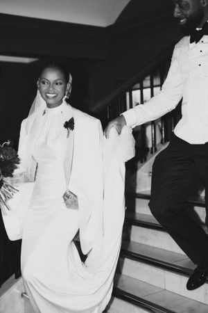 Black and white photo of newlyweds walking down stairs in formal wedding attire.