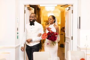 Happy newlyweds entering through doorway with bride holding red bouquet.