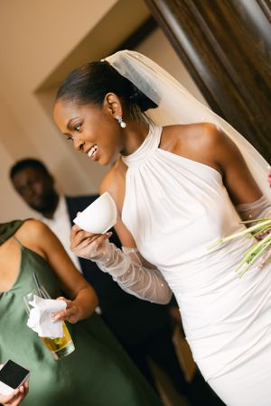 Bride in white halter wedding dress enjoying a drink at reception.
