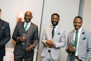 Groomsmen in matching grey suits with green ties enjoying drinks at wedding reception.