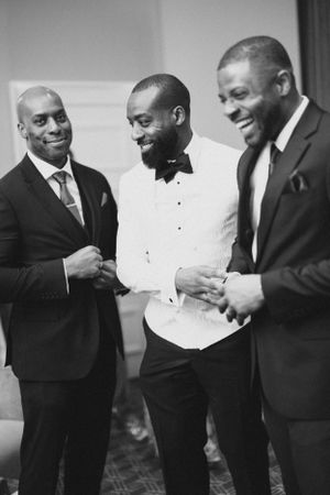 Three men in formal attire share a laugh during a wedding celebration.