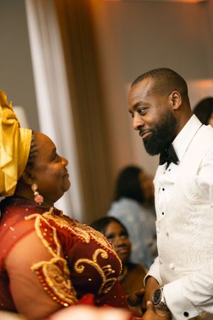 A person in a white tuxedo jacket chats with someone in a gold and red traditional dress.