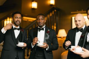Three men in black tie attire enjoy coffee during a formal event.