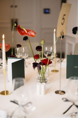 Elegant table setting with red flowers, white candles and numbered table cards at a formal event.