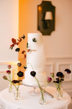 Modern white textured wedding cake decorated with delicate dark florals and greenery.