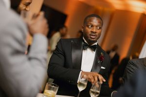 An elegantly dressed guest in a black tuxedo and bowtie enjoys conversation at a formal dinner.