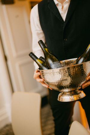 Server in formal attire holding a hammered metallic champagne bowl with wine bottles.